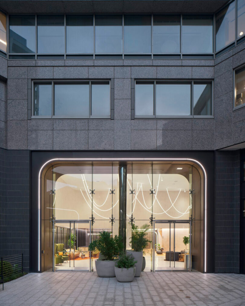 Exterior view of the building entrance showing arched glass doors and glowing interior light fixtures.