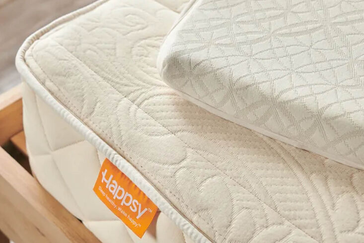 Close-up of a cream-colored organic mattress featuring a brand tag and quilted natural fabric texture.