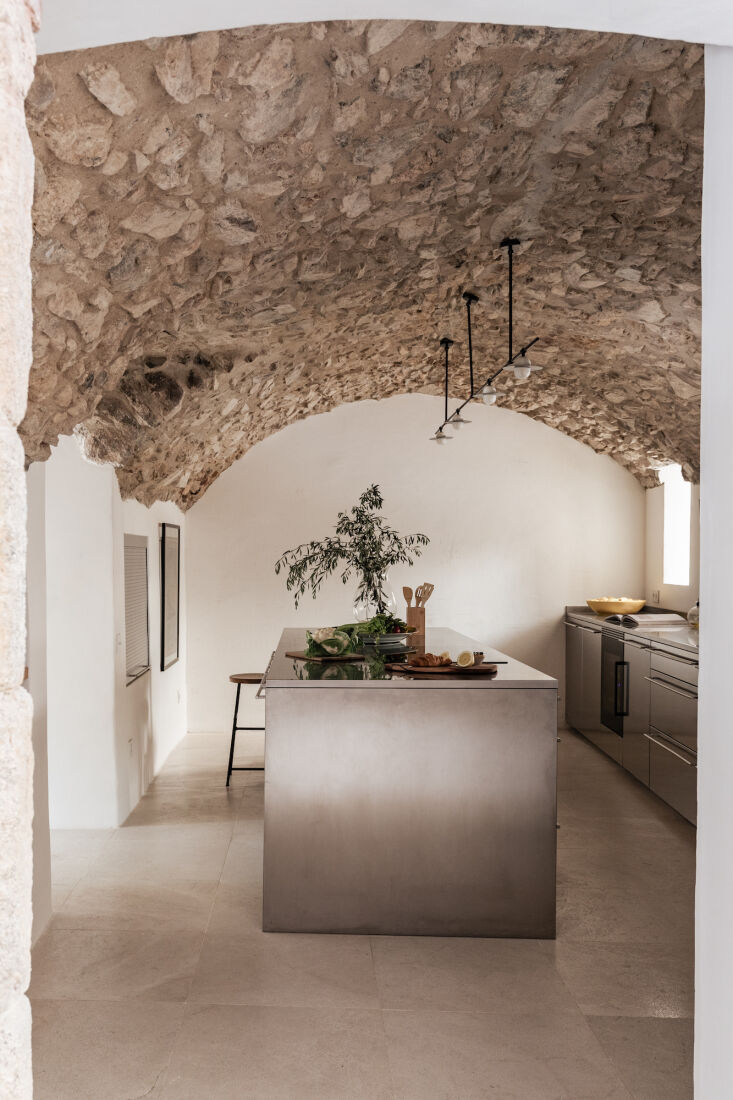 A minimalist Santos stainless steel kitchen island beneath a traditional vaulted brick ceiling.