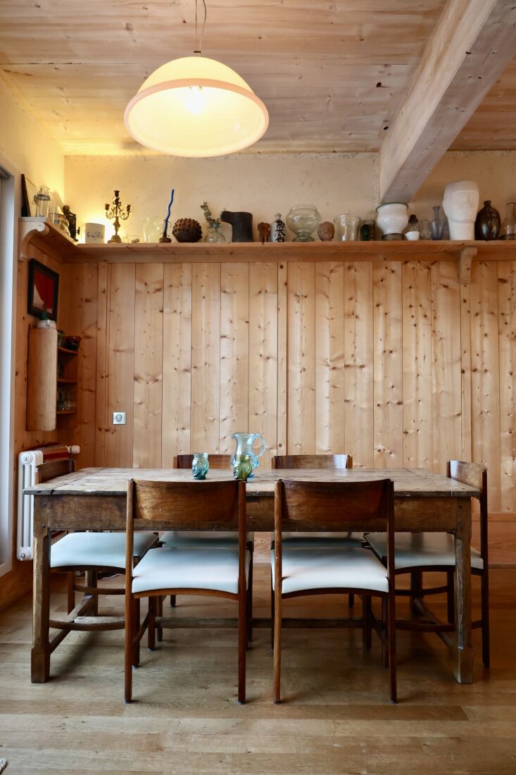 A family dining area with midcentury chairs and a wrap-around bookshelf filled with glass prototypes.