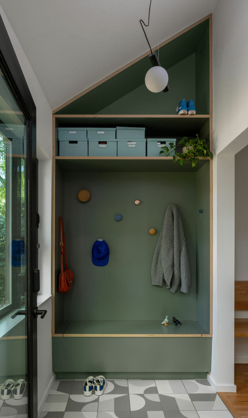 A modern green-toned entryway nook with storage hooks and shelving for coats and shoes.