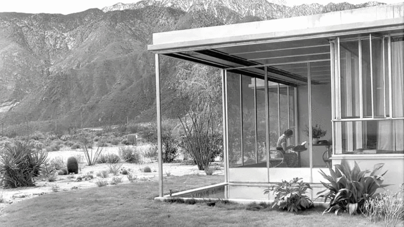 A mid-century modern glass structure with clean metal lines overlooking a desert landscape.