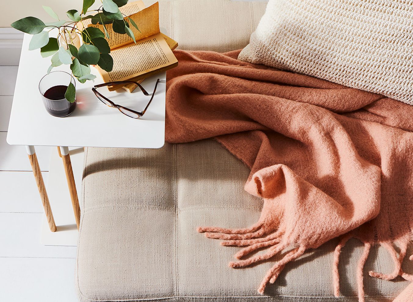 Cozy living room scene with a beige sofa, rust-colored blanket, and natural lighting.