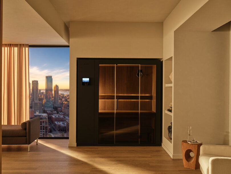 A wooden KLAFS S1 sauna unit in a modern apartment with a sunset city skyline view.