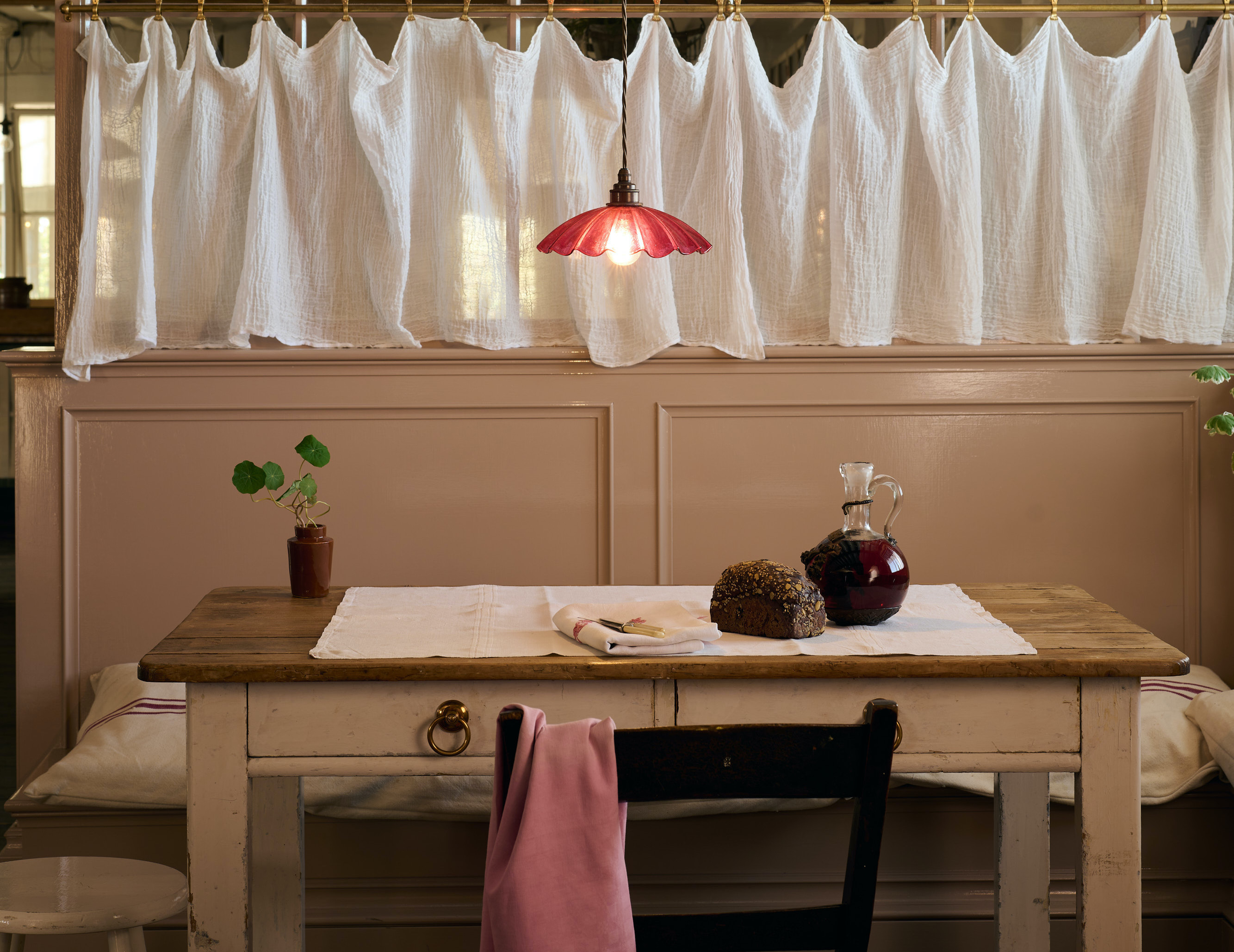 A red frilly glass pendant light over a rustic wooden dining table with vintage breakfast items.