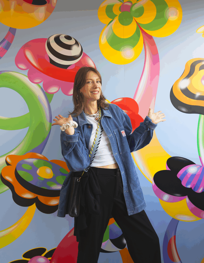 A woman smiling in front of a colorful abstract mural with whimsical shapes.
