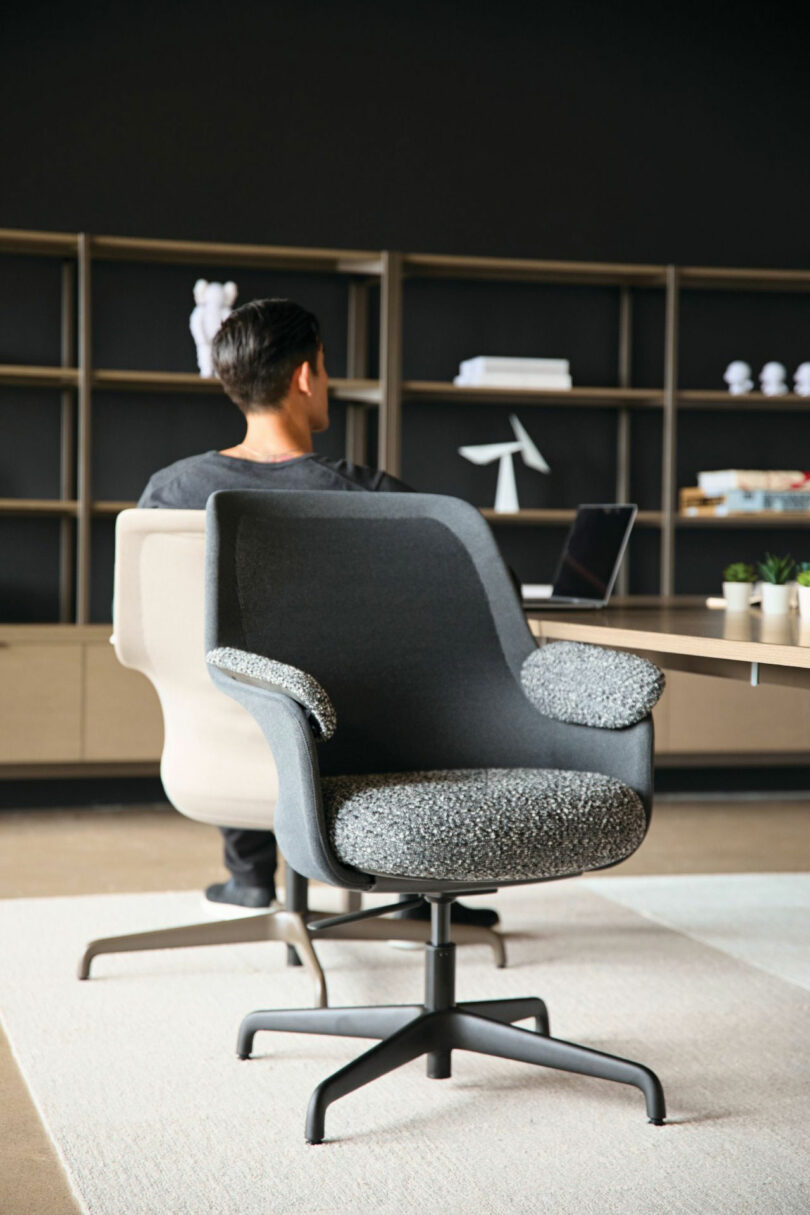 A man working on a laptop while seated in a dark gray textured ergonomic armchair.