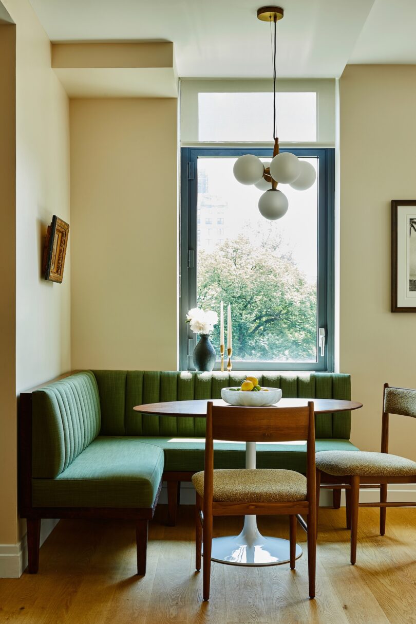 A dining nook with a custom emerald green upholstered banquette and a round wooden table by a window.