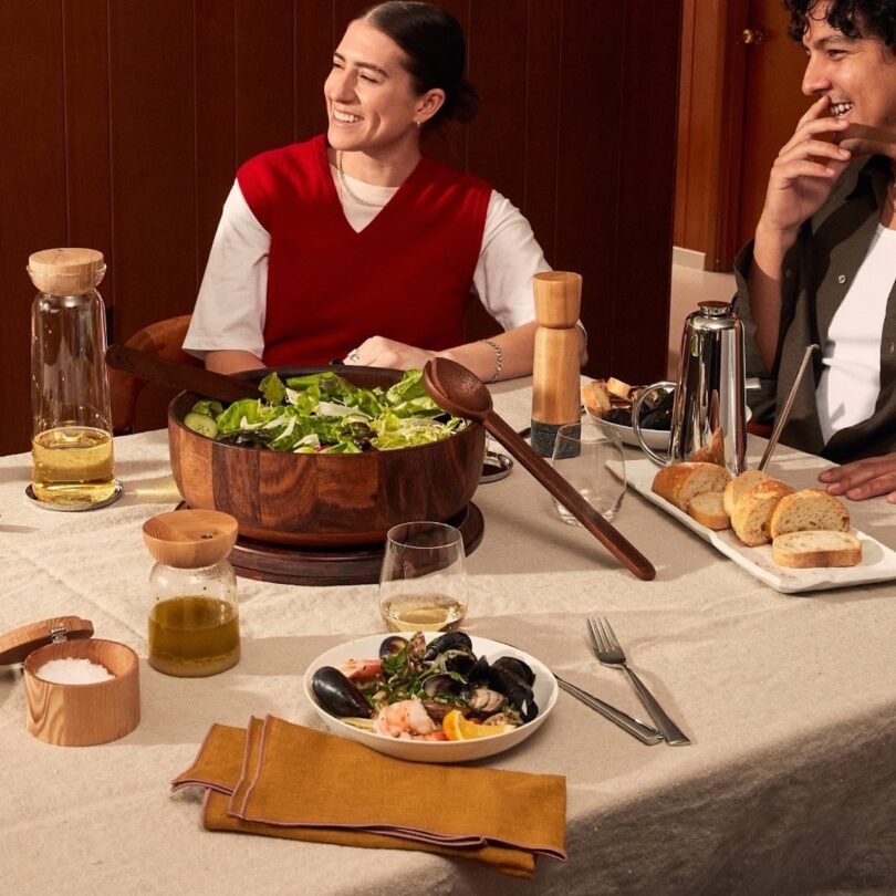 A dining table set with minimalist bowls, bread, and a Mediterranean-style salad.