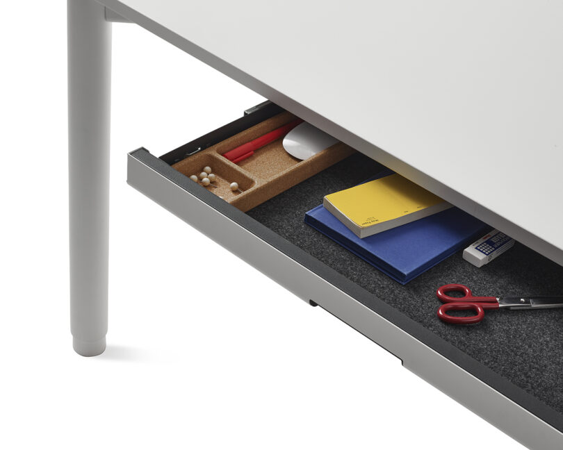 An open under-desk drawer neatly organized with stationery, scissors, and pencils.