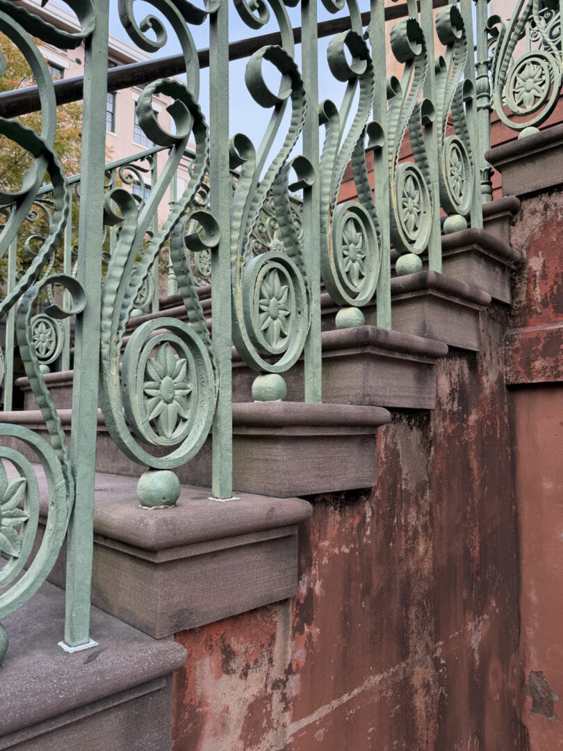 Close-up of an ornate green metal railing on a weathered stone staircase with visible patina.