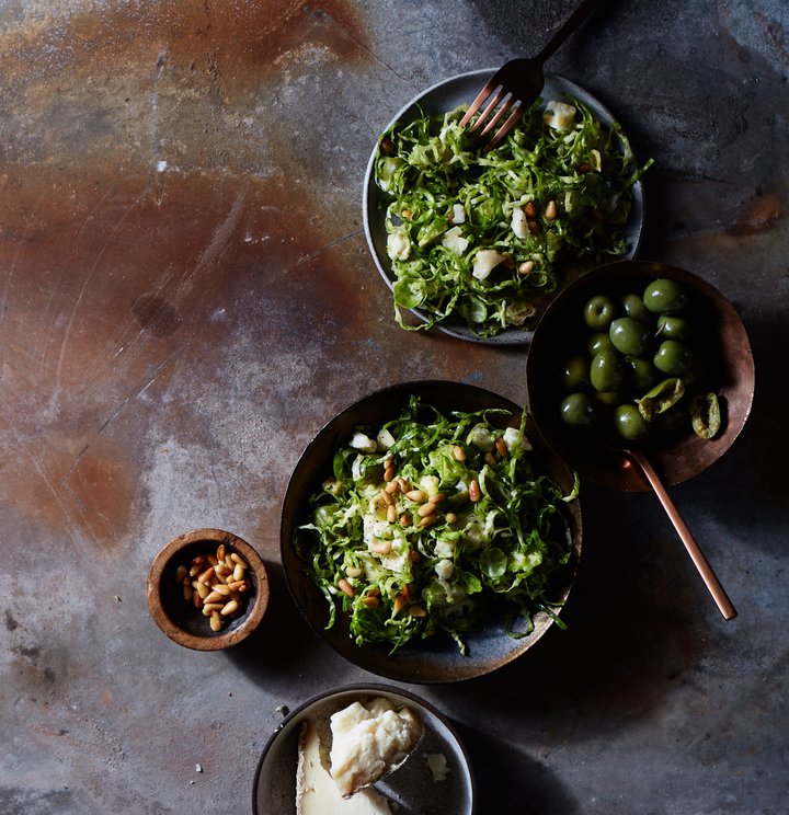 A side dish of shaved Brussels sprouts topped with pine nuts and green olives.