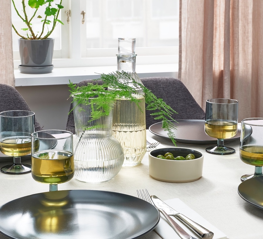 Minimalist table setting with grey plates, textured glassware, and greenery under soft natural light.