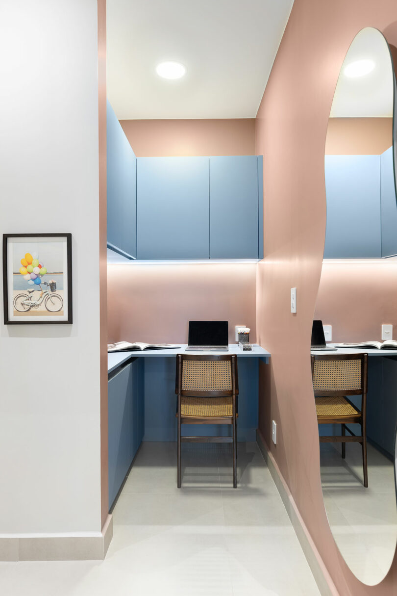 A small modern workspace with blue cabinets, a wooden chair, and a wavy wall mirror.