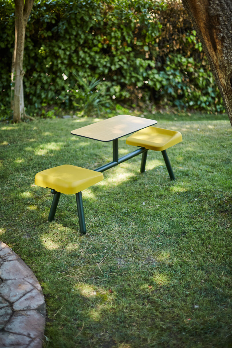 A modern outdoor picnic set with yellow seating and a dark metal frame on a green lawn.