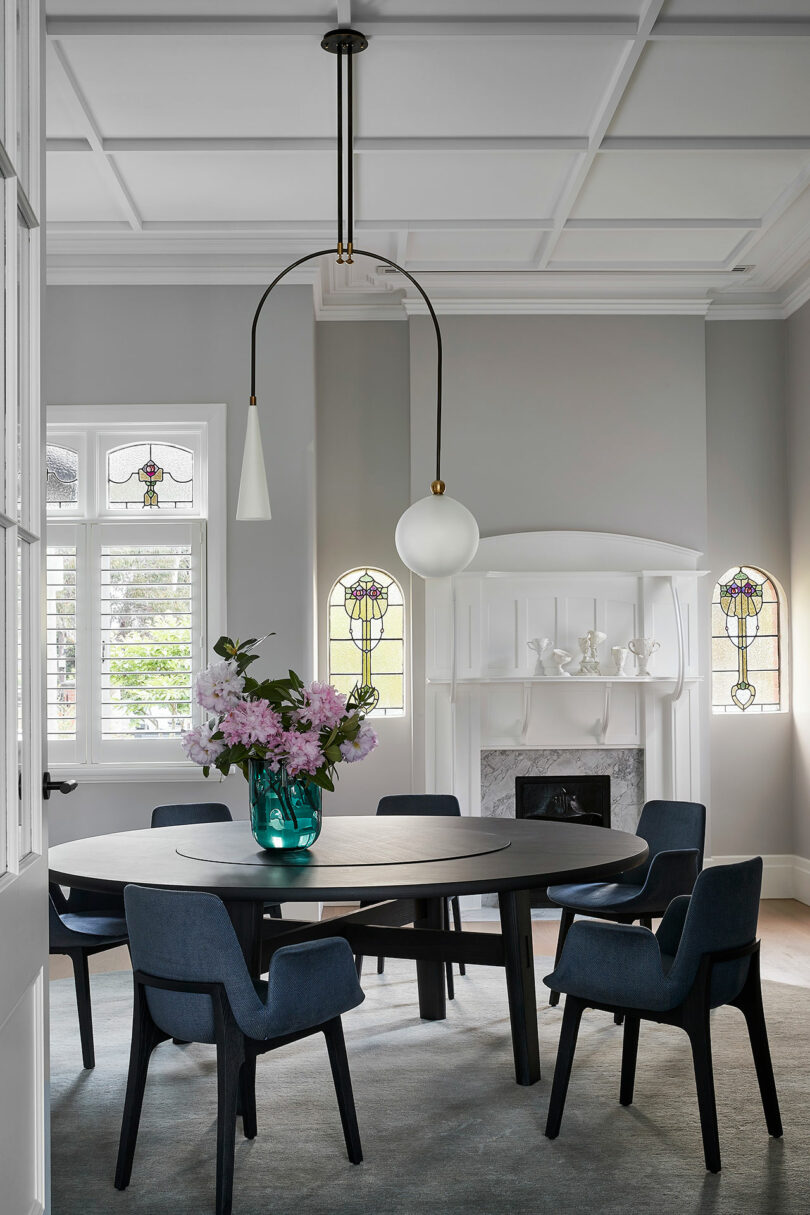 Dining room with a black round table, blue chairs, and a white heritage fireplace with stained glass.