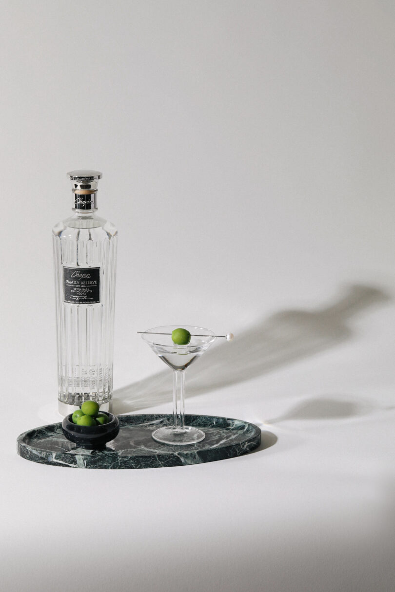 A bottle of spirits and a prepared martini on a luxurious green marble tray.