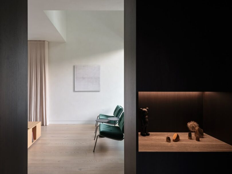 Minimalist living area with sage green chairs, warm beige walls, and wood flooring.