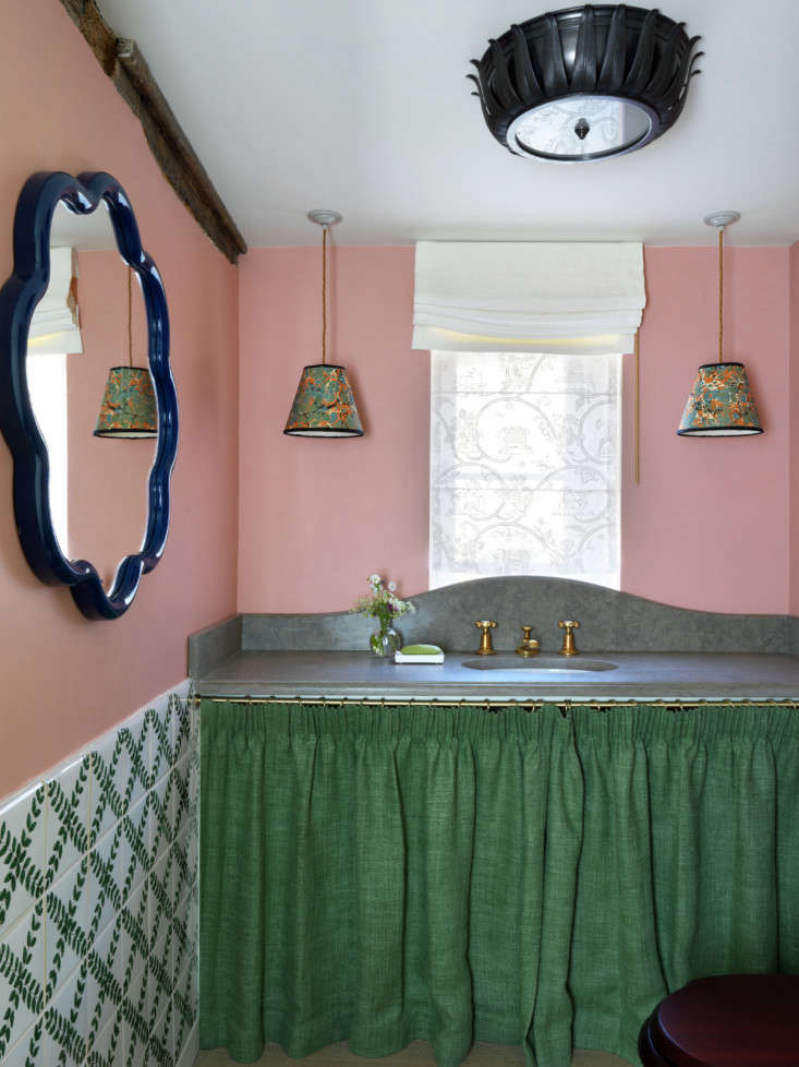 Maximalist powder room with patterned wallpaper, a sink skirt, and a colored mirror.