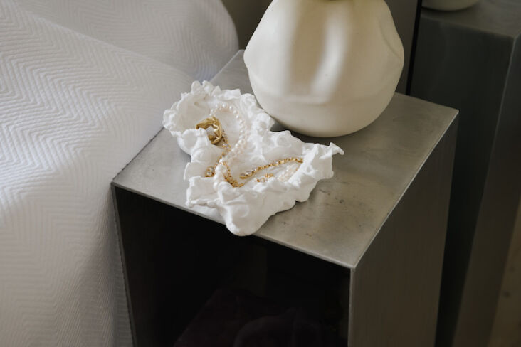 Aluminum bedside table with a ruffled ceramic tray and gold jewelry.