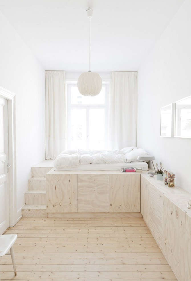 Minimalist bedroom featuring a light wood platform bed with integrated storage drawers and white linens.