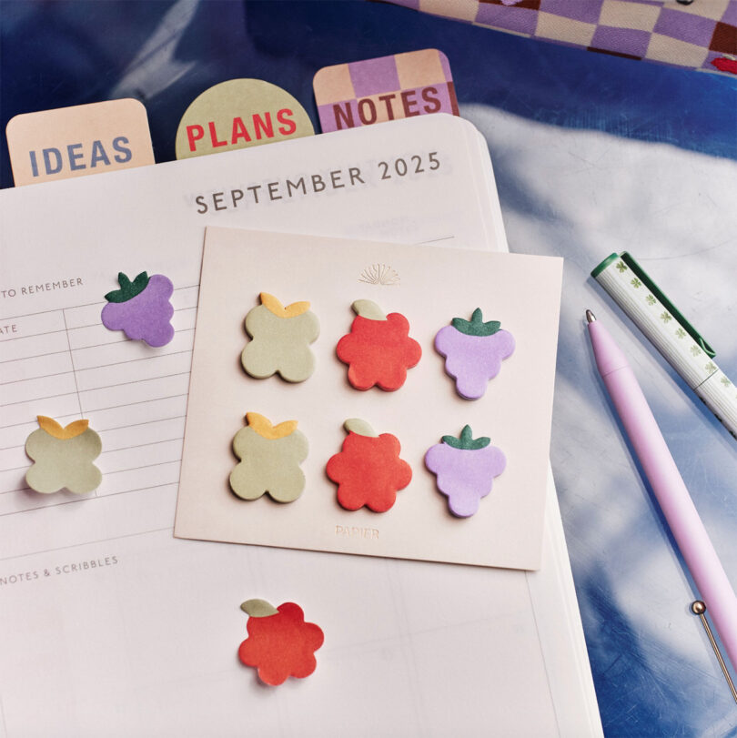 Top-down view of an open 2025 planner with fruit-shaped sticky notes and stationery accessories.