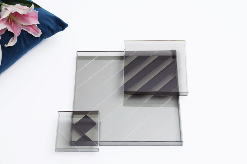 Transparent geometric trays on a white table next to pink lilies and a blue cushion in a home setting.