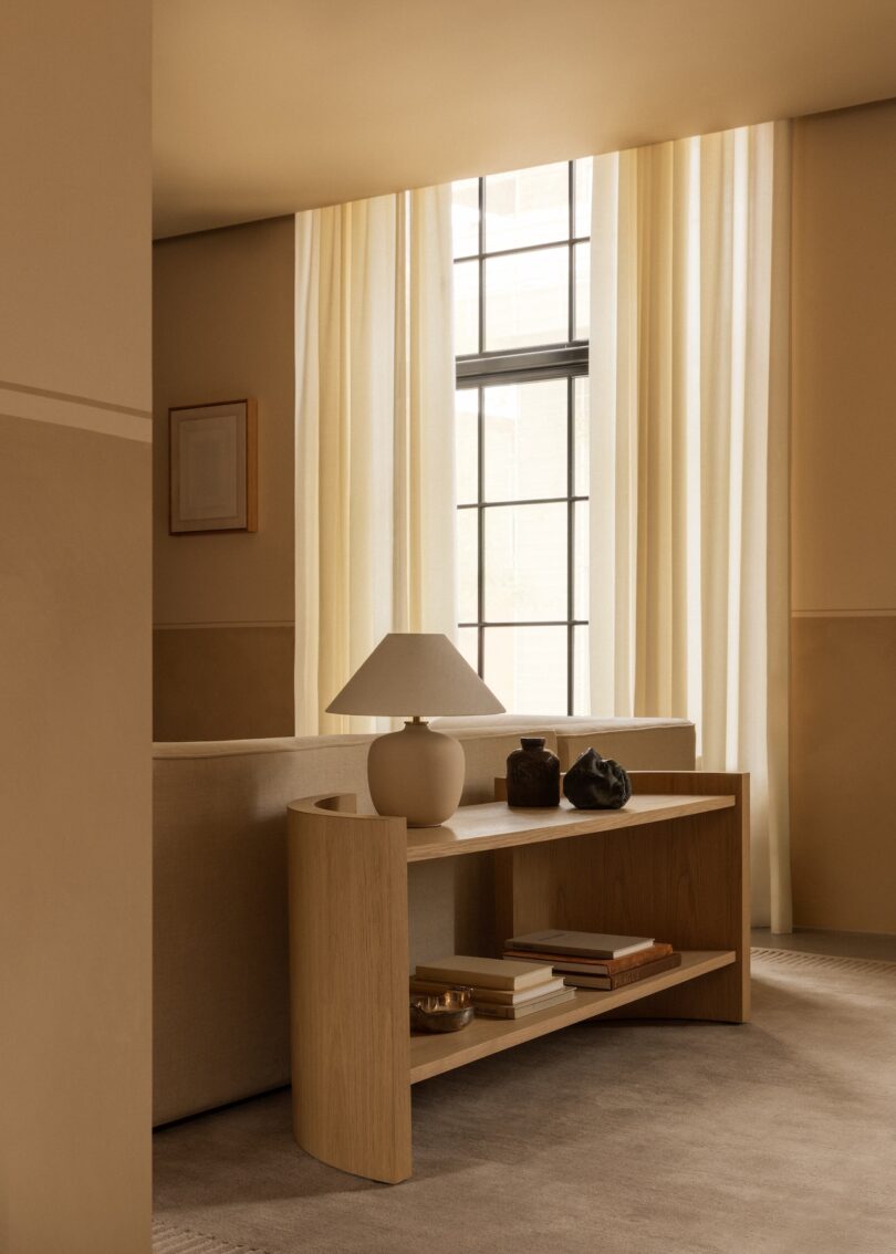 A low oak console table styled with a lamp and books behind a beige sofa.