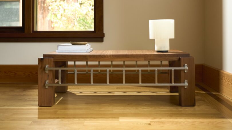 A low wooden coffee table with horizontal metal bars across the front, styled with books and a lamp.