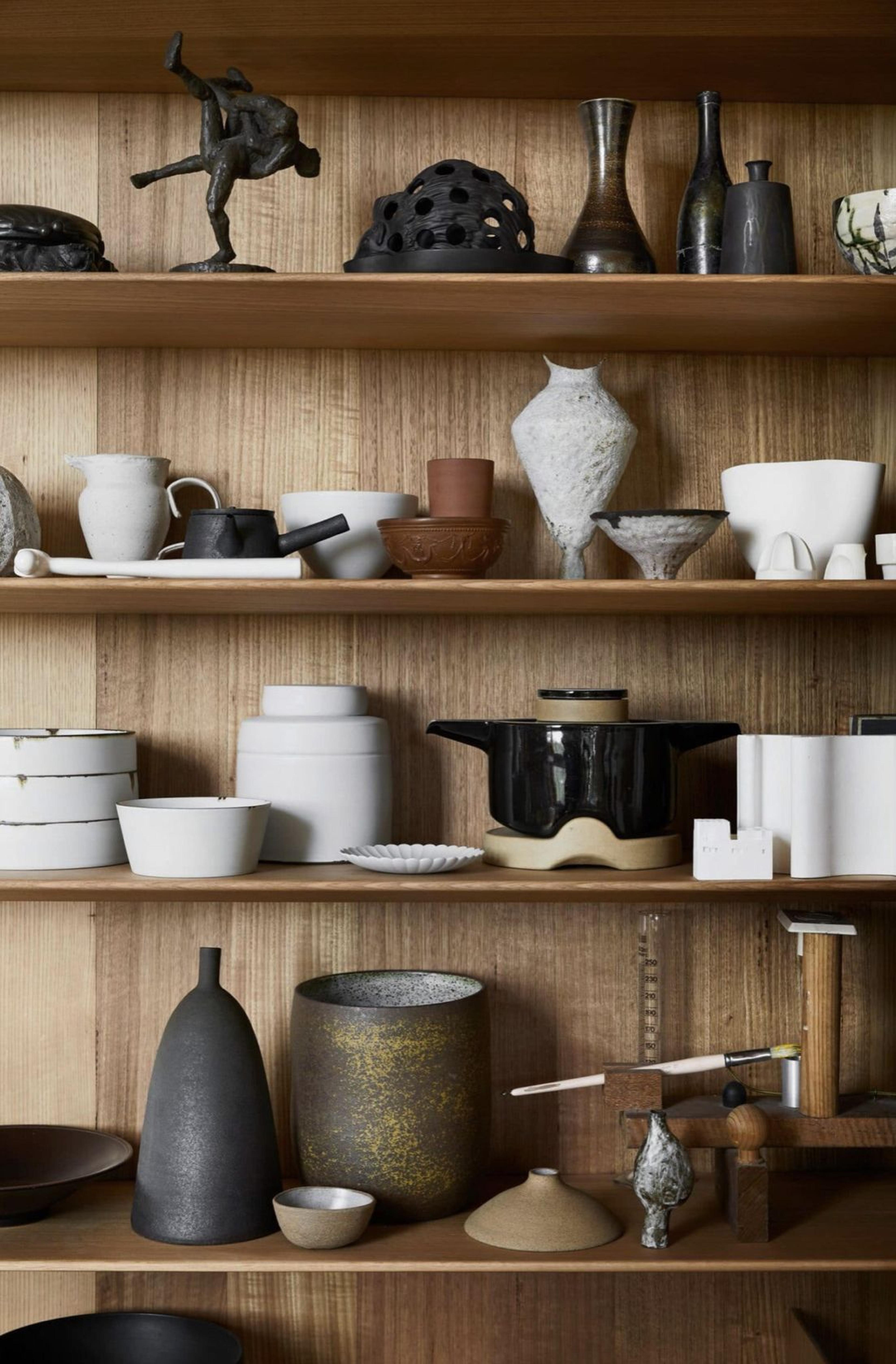 Artisanal pottery lined up neatly on minimalist wooden wall shelves.