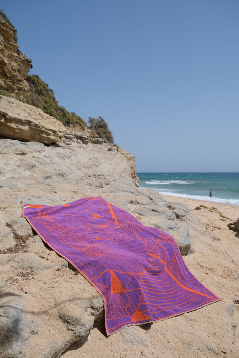 A purple and orange patterned beach towel spread across a rocky coastal cliff overlooking the ocean.