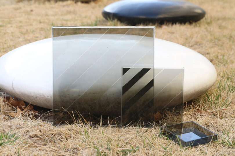 Glass panels and a small tray placed on dry grass in front of smooth black and white stones.
