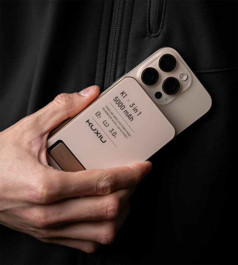 A hand holding the Kuxiu 5000mAh power bank attached to a smartphone, showing the clean branding and compact size.