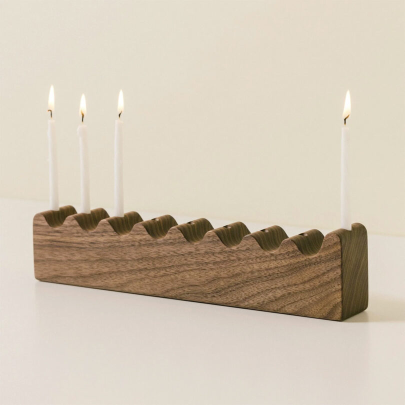 A minimalist wood block menorah with a wavy top design and natural grain patterns.