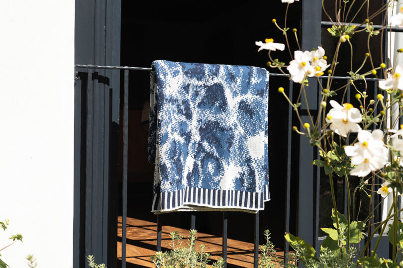 A blue and white patterned blanket with striped edges hanging on a black metal railing.