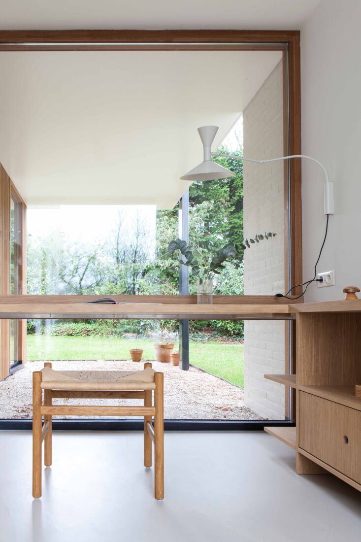 A minimalist home office desk positioned next to a large window overlooking a garden.
