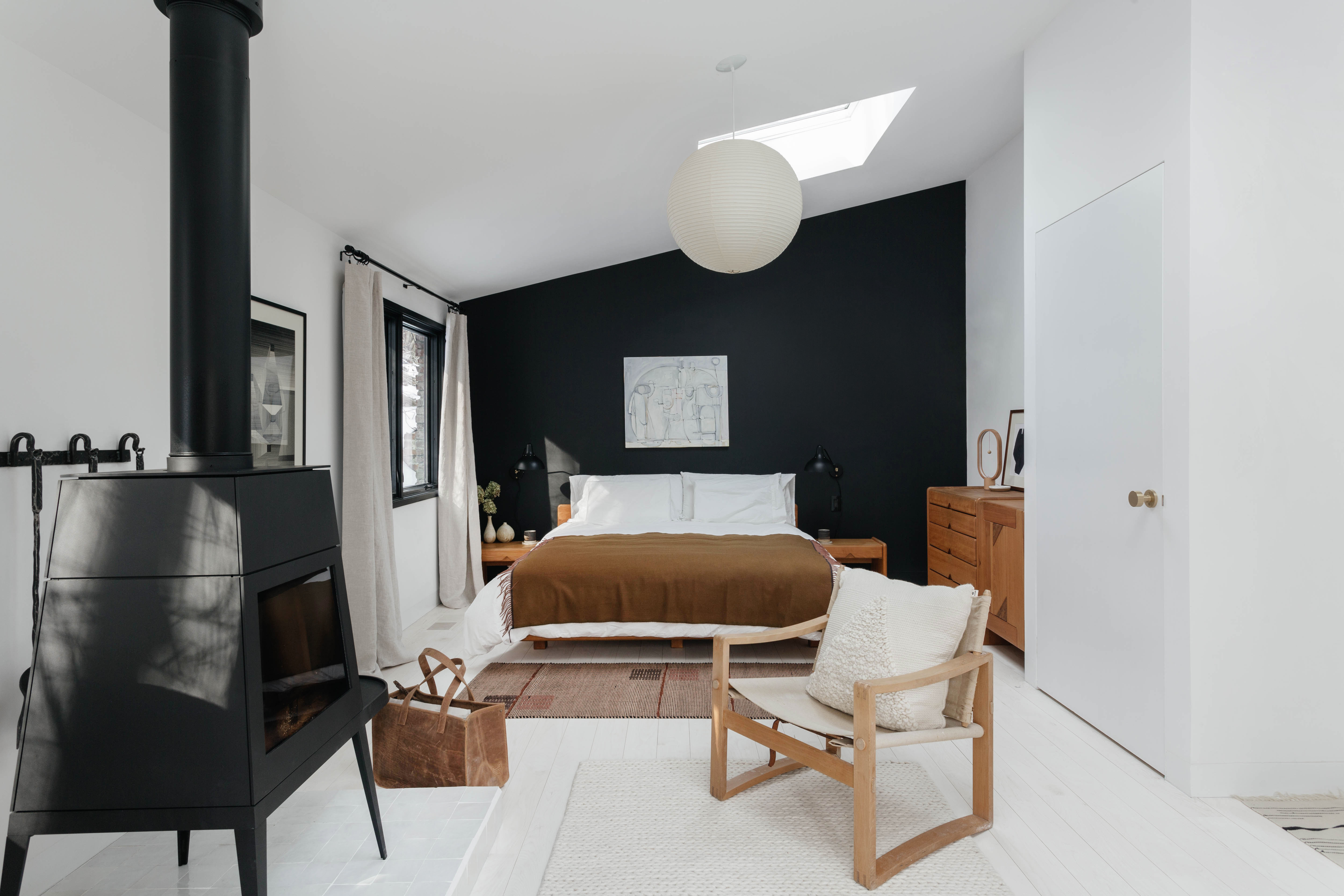 Minimalist bedroom with a skylight, black accent wall, and a traditional wood-burning stove.