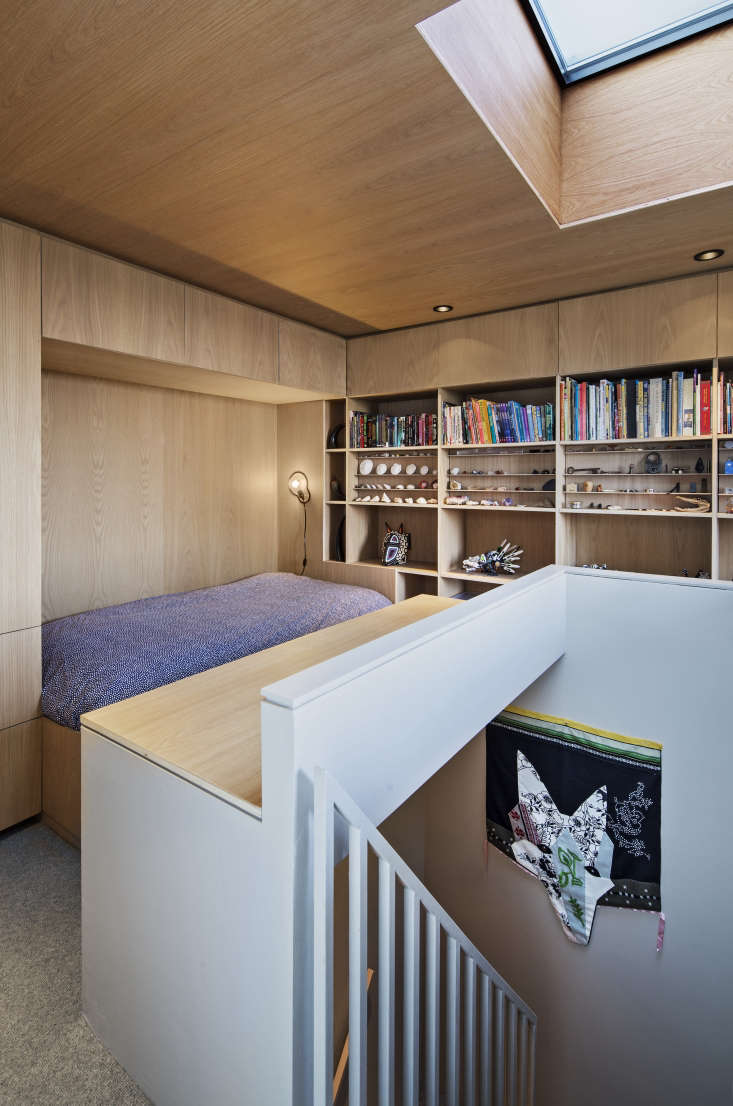 Loft bedroom with custom white oak plywood shelving and integrated bed design under a skylight.