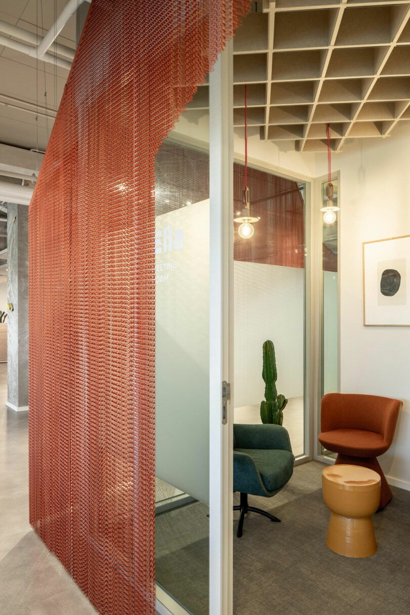 Office nook with a red mesh curtain, colorful chairs, and a potted cactus.