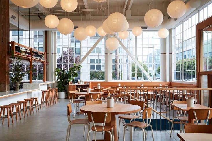 A large cluster of various Noguchi Akari lanterns hanging in a high-ceilinged dining space.
