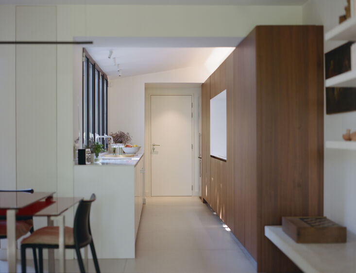 A minimalist kitchen island and cabinetry made of rich, warm exotic wood in an open-plan layout.