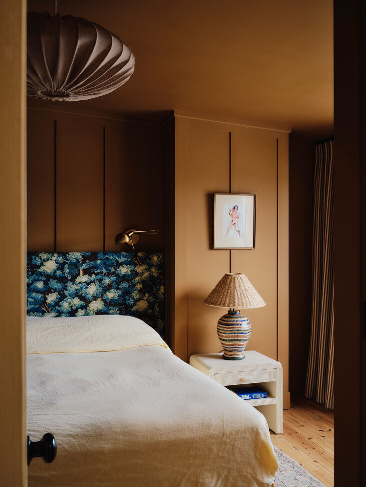 A bedroom with terracotta walls, a floral headboard, and a woven pendant light creating a warm atmosphere.