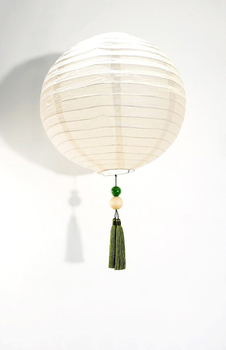 A minimalist white paper lantern with green and cream beads and a green tassel.
