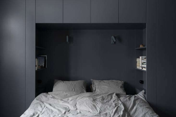 A bed nestled into a deep nook created by a full wall of white storage cabinets.