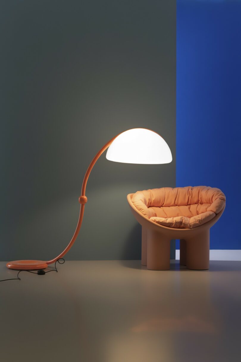 An orange Serpente floor lamp paired with a matching orange plush chair against a teal wall.