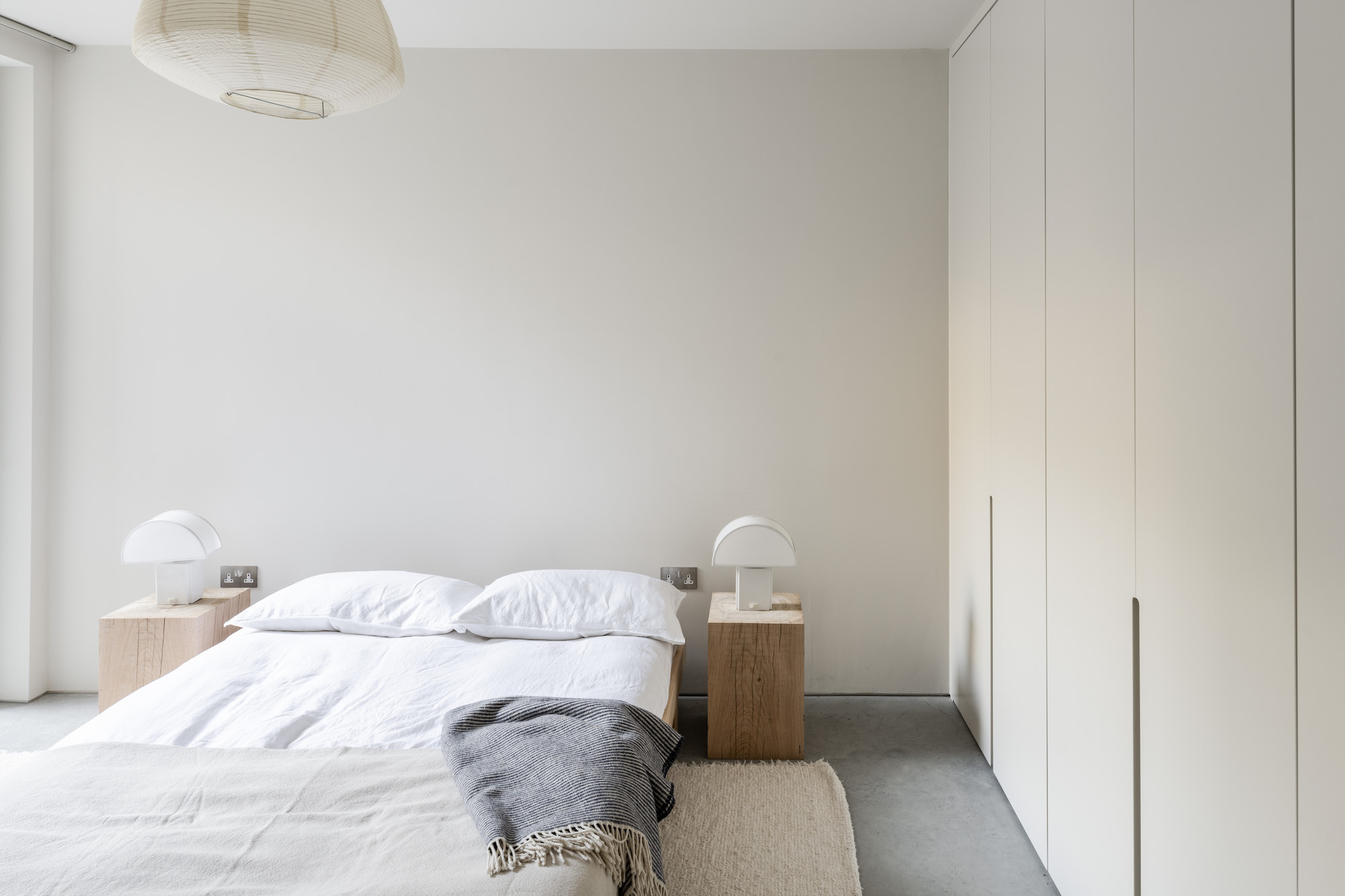 Wide shot of an intentionally simple bedroom with a low bed and neutral tones.