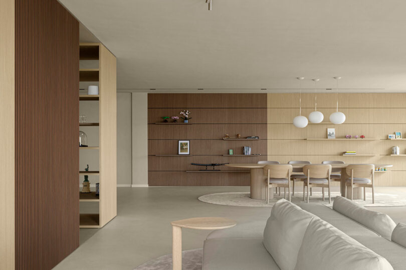 Modern open-plan living and dining area with neutral tones, featuring floating shelves and spherical pendant lights.