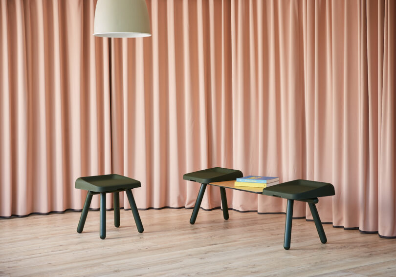 Dark green modular seating set against soft pink curtains in a minimalist interior space.