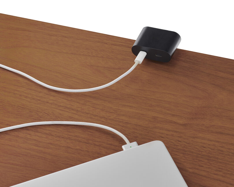 A close-up of a laptop plugged into a USB-C port integrated into the wooden surface of the desk.