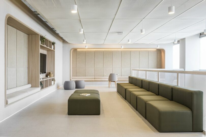 A lounge area featuring modular green seating and a central ottoman against a backdrop of soft lighting and shelving.